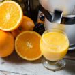 Bedste slow juicer med friske appelsiner, nogle hele og nogle halverede, som ligger på et rustikt træbord