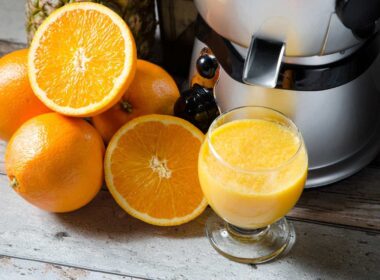 Bedste slow juicer med friske appelsiner, nogle hele og nogle halverede, som ligger på et rustikt træbord