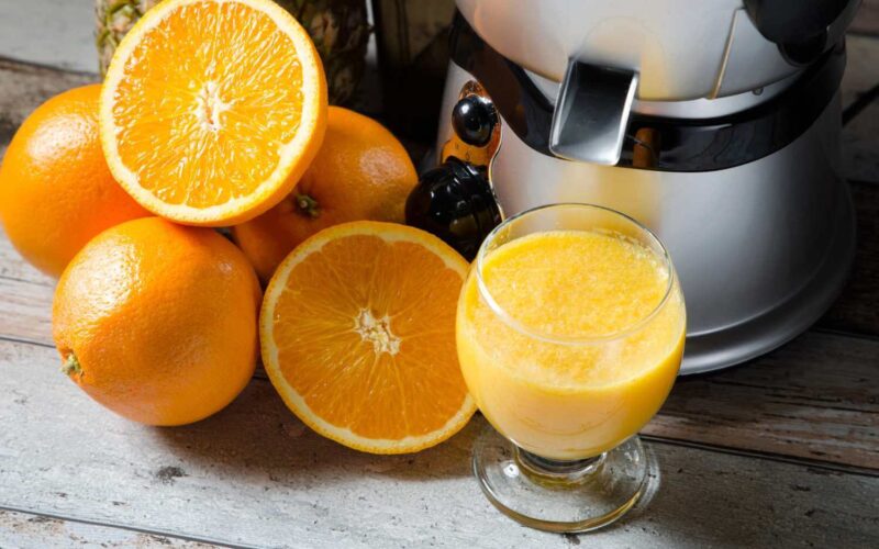Bedste slow juicer med friske appelsiner, nogle hele og nogle halverede, som ligger på et rustikt træbord