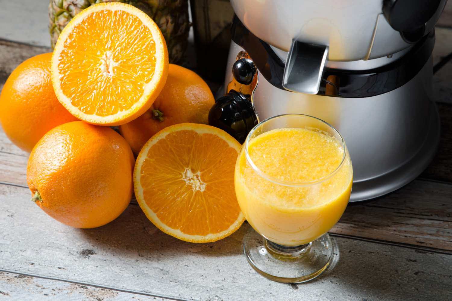 Bedste slow juicer med friske appelsiner, nogle hele og nogle halverede, som ligger på et rustikt træbord
