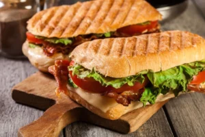 Panini grill med sandwich, tomat, ost og salat på et træskærebræt