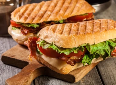 Panini grill med sandwich, tomat, ost og salat på et træskærebræt