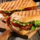 Panini grill med sandwich, tomat, ost og salat på et træskærebræt